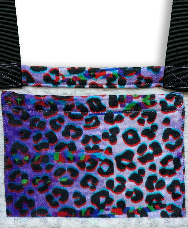 Immagine still life di una borsa leopardata aperta su sfondo viola, rivelando una tasca interna con la stessa stampa. Il dettaglio della tasca interna evidenzia la funzionalità e il design curato della borsa, che unisce stile e praticità